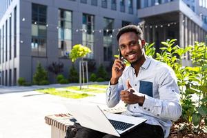 Successful African American businessman works with laptop and talks on the phone, looks photo