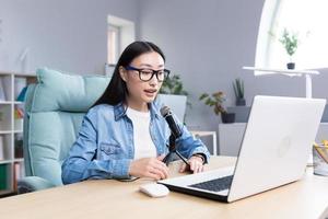 Young beautiful Asian woman recording audio podcast, woman in office using professional microphone photo