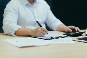 Close-up photo. The hands of a young man who works at a desk with documents, a calculator, writes photo