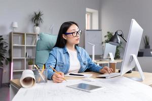 asiático mujer arquitecto diseñador trabajando a escritorio computadora, dibujo con lápiz,trabajando en proyecto foto