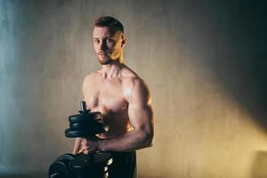 Male blond athlete lifts dumbbells with hand on biceps studio photo with raindrops