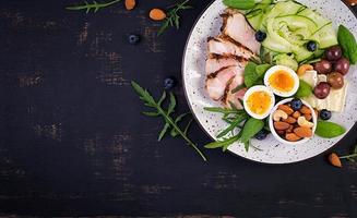 Ketogenic diet. Keto brunch. Boiled egg, pork steak and olives, cucumber, spinach, brie cheese, nuts and blueberry. Top view photo