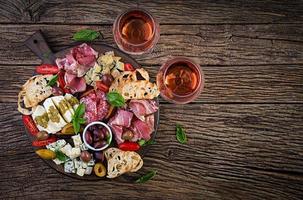 Antipasto platter with ham, prosciutto, salami, blue cheese, mozzarella with pesto and olives on a wooden background. Top view, overhead photo