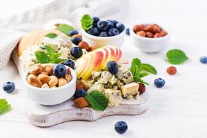 Cheese platter with assorted cheeses, blueberry, apples, nuts on white table. Italian cheese  platter and fruit. photo