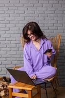 Beautiful businesswoman working on a laptop in a chair near the window. Female freelancer connecting to internet via computer. Blogger or journalist writing new article. photo