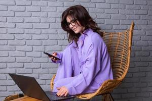 Beautiful businesswoman working on a laptop in a chair near the window. Female freelancer connecting to internet via computer. Blogger or journalist writing new article. photo