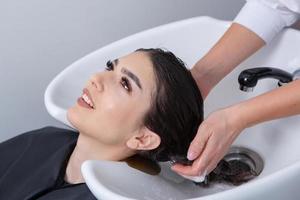 peluquero profesional lavando el cabello de una mujer joven en un salón de belleza. primer plano del cabello de la mujer en el salón de belleza, concepto de peinado foto