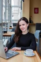 Beautiful businesswoman working on laptop in coffee shop. Female freelancer connecting to internet via computer. Blogger or journalist writing new article. photo