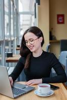 bella mujer de negocios trabajando en una laptop en una cafetería. mujer independiente que se conecta a internet a través de la computadora. blogger o periodista escribiendo un nuevo artículo. foto