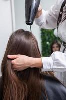 Young woman combing her long dark hair with a comb in a beauty salon. A straight healthy brunette hair that has undergone the hair straightening procedure. photo