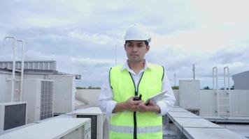 asiático mantenimiento ingeniero trabajos en el techo de fábrica. contratista inspeccionar compresor sistema y planes instalación de aire condición sistemas en construcción. tecnología, en línea comprobación video