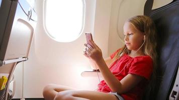 Adorable little girl traveling by an airplane sitting near window. Kid listening music sitting near aircraft window video