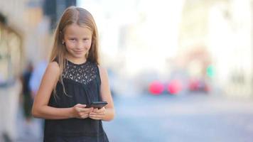 förtjusande liten flicka med smart telefon på värma dag utomhus i europeisk stad video