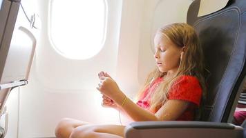 Adorable little girl traveling by an airplane. Kid listening music sitting near aircraft window video