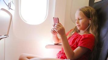 Adorable little girl traveling by an airplane sitting near window. Kid listening music sitting near aircraft window video