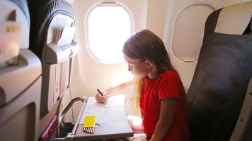 Adorable little girl traveling by an airplane. Kid drawing picture with colorful pencils sitting near aircraft window video