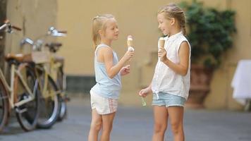 adorable pequeño muchachas comiendo helado al aire libre a verano. linda niños disfrutando real italiano helado cerca heladería en Roma video
