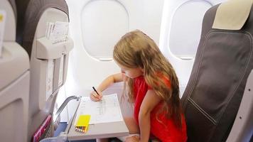 adorable petite fille voyageant en avion. enfant dessinant une photo avec des crayons colorés assis près de la fenêtre de l'avion video