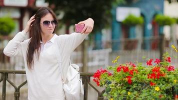 Young woman taking self portrait backround beautiful house in european city. Caucasian tourist enjoy her european summer vacation in Europe. video