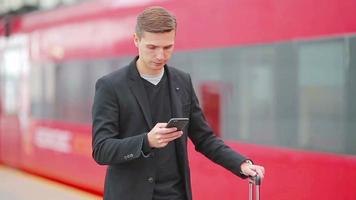 Young caucasian man with smarphone and luggage at station traveling by train video