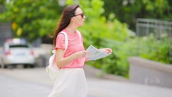 Happy young woman with map walking along city street in Europe asking help another caucasian girl video