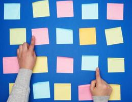 two female hands and a lot of empty paper multi-colored square stickers on a blue background photo