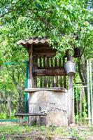 Old well with iron bucket on long forged chain for clean drinking water photo