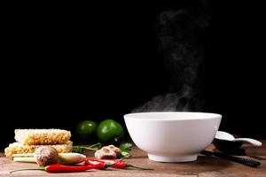 a bowl of instant noodles or pasta Delicious hot soup, Thai, Chinese, Japanese food with chopsticks and condiments, lime, chili, shiitake mushrooms, arranged on table isolated on black background. photo