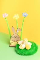 Wooden bunny, yarn flowers, round decorative grass carpet with textured Easter eggs on yellow-green. photo