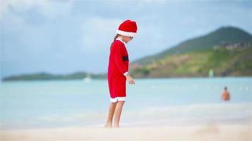 adorable chica con sombrero de navidad en la playa blanca durante las vacaciones de navidad video