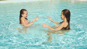 adorable pequeño muchachas jugando juntos y teniendo divertido en al aire libre nadando piscina video