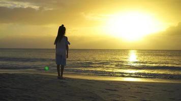 Adorable happy little girl walking on white beach at sunset. video