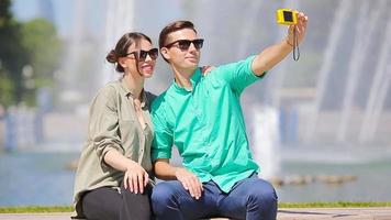 joven turista Pareja de viaje en Días festivos en Europa sonriente contento. caucásico amigos tomando selfie en parque antecedentes grande fuente video