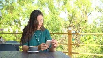 mulher com smartphone no café bebendo café sorrindo e mensagens de texto no celular. retrato de uma linda jovem video