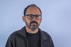 retrato de un hombre barbudo de 60 años de fondo azul con sombrero y gafas foto