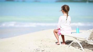 pequeno menina desfrutando em espreguiçadeira em branco de praia video