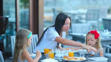 Madre joven y adorables niñas desayunando en la cafetería al aire libre video