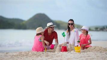 familia de cuatro haciendo castillos de arena en la playa blanca tropical
