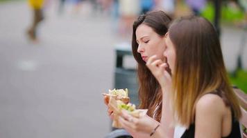mulheres caucasianas come sanduíche de fast-food de hambúrguer na rua ao ar livre. meninas ativas com fome e comendo comida de rua depois de longa caminhada video