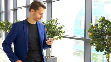 Urban businessman talking on smart phone inside in airport. Casual young boy wearing suit jacket. Caucasian man with cellphone at the airport while waiting for boarding video