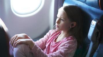 Adorable little girl traveling by an airplane. Cute kid sitting near window in aircraft video