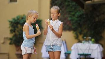 adorable pequeño muchachas comiendo helado al aire libre a verano. linda niños disfrutando real italiano helado cerca heladería en Roma video