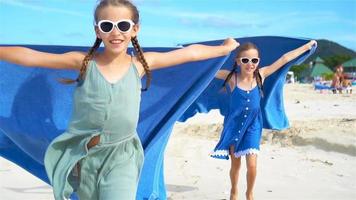 Little girls have fun with beach towel during tropical vacation