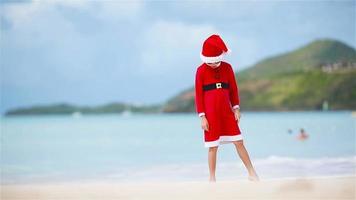 poco ragazza nel Natale cappello su bianca spiaggia durante natale vacanza video