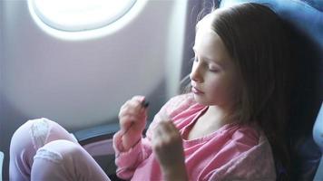 bezaubernd wenig Mädchen Reisen durch ein Flugzeug. süß Kind Aufpassen Film in der Nähe von Fenster im Flugzeug. schleppend Bewegung video