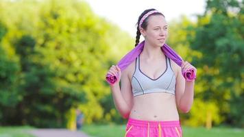 Beautiful young sport woman with towel. Portrait young smiling fit woman with white towel resting after workout sport exercises outdoors on a background of park trees. video