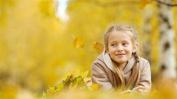 Portrait of adorable little girl with yellow leaves bouquet in fall. Beautiful smiling kid lying on leaves carpet video