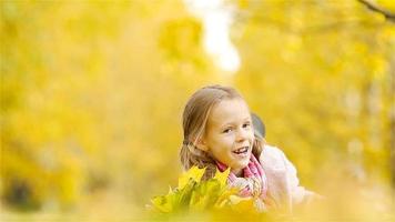 Portrait of adorable little girl with yellow leaves bouquet in fall. Beautiful smiling kid lying on leaves carpet video