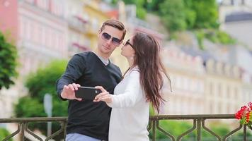 romantisch paar wandelen samen en nemen selfie in Europa. gelukkig geliefden genieten van stadsgezicht met beroemd oriëntatiepunten. elegant stedelijk jong Mens en vrouw met rugzakken Aan reizen. video