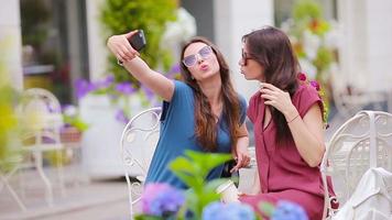 zwei jung Mädchen nehmen Selfie durch Clever Telefon beim das draußen Cafe. video